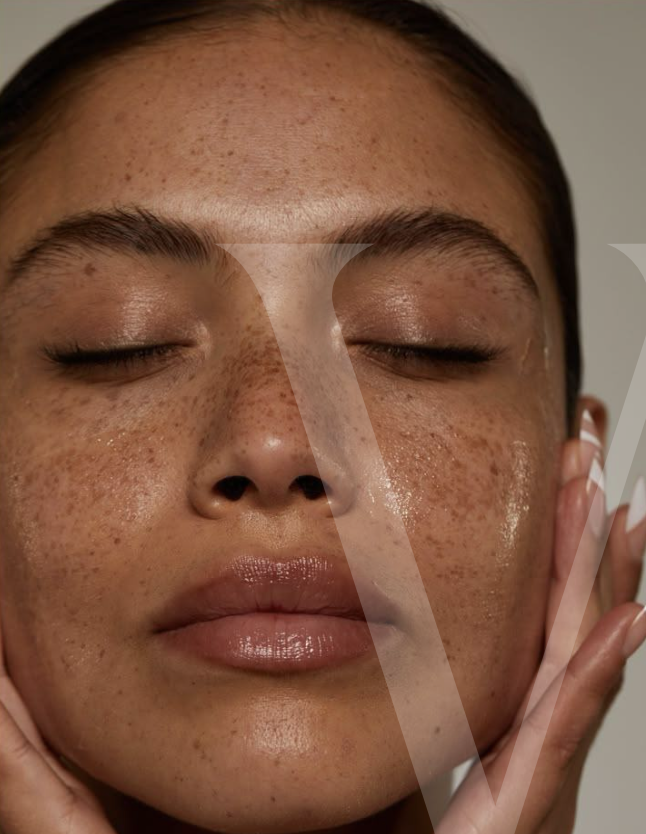 Primer plano artístico de mujer joven con piel luminosa y saludable, ojos cerrados, expresión serena, realizando una suave rutina facial. Imagen minimalista y cálida que representa el cuidado natural y consciente promovido por Véora.